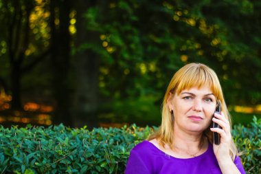 Defocus Kafkas sarışın kadın konuşuyor, dışarıda, dışarıda konuşuyor. Mor bluzlu 40 'lı yaşlarda bir kadın bankta oturuyor. Yetişkin bir kadın cep telefonu kullanıyor. Uzayı kopyala Odaklanamıyorum.