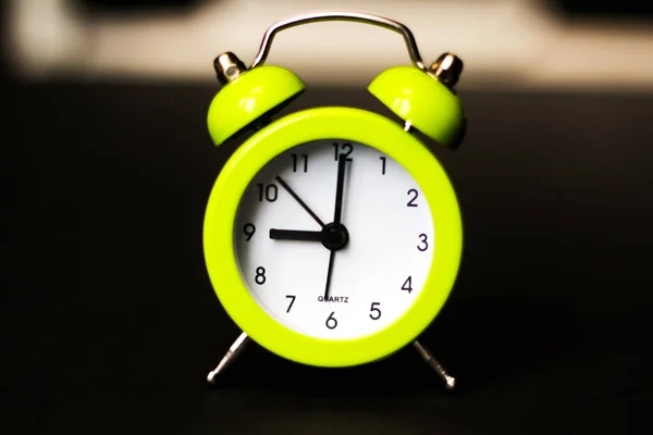 Light green alarm clock on a black background. Back to school. Time minimalistic concept. At nine o'clock in the morning Selective focus.