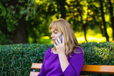Defocus Kafkas sarışın kadın konuşuyor, dışarıda, dışarıda konuşuyor. Mor bluzlu 40 'lı yaşlarda bir kadın bankta oturuyor. Yetişkin insan cep telefonu kullanıyor, akıllı telefon. Odaklanamıyorum.