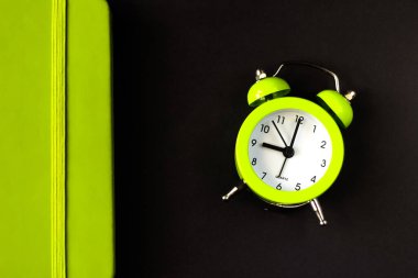 Çalar saat sabah uyanma zamanı. Siyah arka planda açık yeşil alarm saati ve defter. Zaman minimalist kavramı. Sabahın dokuzunda Seçici odak.