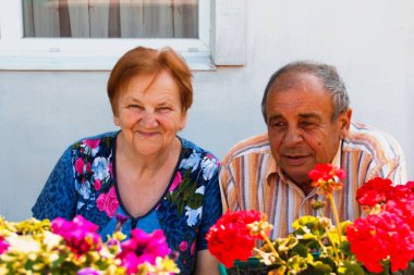 Yaz günü gülümseyen yaşlı bir çift. Çiçek bahçesinde oturan neşeli, yaşlı bir çift karı koca. Aşk ve aile kavramı.