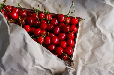 Kutunun bir parçası, arka planda buruşuk kağıt kaplamalı kuyruklu tatlı kırmızı kirazlar. Yaz meyveleri ve meyveler. Hasat ve hasat konsepti. Organik yiyecekler. Üst Manzara. Çapraz. Yakın plan..