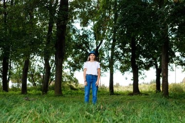 Açık havada şapka takan, kahverengi saçlı, ciddi bir genç kadının genel portresi. Yeşil doğa ağaçları arka plan, orman. Kameraya bakıyorum. Odaklanamıyorum.