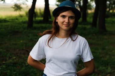 Kahverengi saçlı, açık havada şapka takan mutlu, gülümseyen genç bir kadının defocus portresi. Yeşil doğa geçmişi. Kameraya bakıyorum. Dark Park 'ta duran kadınlar. Odaklanamıyorum.