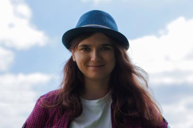 Defocus, kahverengi saçlı, gülümseyen güzel bir genç kadının dış görünüşünü yakından çek ve dışarıdaki kameraya bak. Gökyüzü bulutları. Odaklanamıyorum.