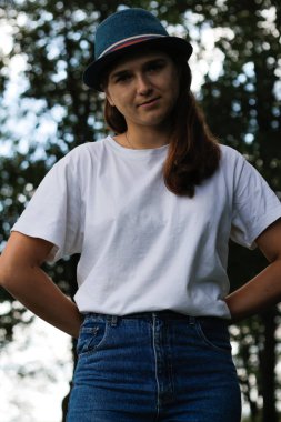 Kahverengi saçlı, açık havada şapka takan üzgün genç bir kadının Defocus portresi. Yeşil doğa geçmişi. Kameraya bakıyorum. Dark Park 'ta duran kadınlar. Dikey. Odaklanamıyorum.