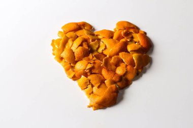 Kurumuş portakal ve mandalina kabuklarından yapılmış bir kalp. Beyaz bir arka planda. Bir sürü küçük kurumuş portakal kabuğu kalp şeklinde serilmişti. Aşk sembolü. Sevgililer Günü. Seçici odak.