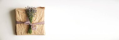 A charming gift or present wrapped in simple eco-friendly paper. The small box hints at a delightful surprise, birthday or the holiday season. Lavender flower. White background with copy space.