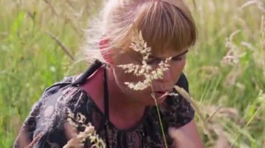 Yüksek çimde oturan ve çilek yiyen defocus kadın. Çilek kokusunun tadını çıkar. Yaz yemeği. Zenginlik ve doğaya yakınlık Odaklanamaz.