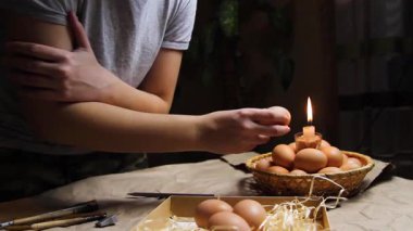 Genç bir kadın alevin yanında yumurtayı tutuyor ve ısıtıyor. Folk tasarımlarıyla süslenmiş Ukrayna Paskalya yumurtalarını boyamaya hazırlanıyorlar. Pysanka, Paskalya yumurtası. İyi geceler. El yapımı..