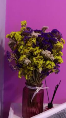 Still Life, Pembe Kurumuş Çiçekler Vazoda ve Aroma Diffuser. Kırmızı arka planda kurumuş sarı ve mavi çiçekli cam bir vazonun olduğu şık, sakin bir hayat..