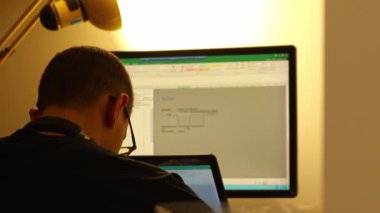 Masada çalışan adamın Excel hesap tablosu ve dizüstü bilgisayarını gösteren geniş ekranlı görüntüsü. Odaklanmış ofis işleri. Erkek bir muhasebeci hesap tablolarında bir bilgisayarın başında çalışıyor..