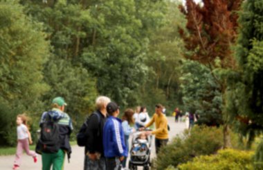 Çocuklu aileler de dahil olmak üzere insanların bulanık görüntüsü yemyeşil bir parkta ya da botanik bahçesinde yürüyor. Parkta yürüyen insanlar arka planda bulanık.