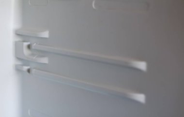 Buzdolabının beyaz plastik iç duvarının yakın plan, bulanık bir görüntüsü, rafları tutmak için tasarlanmış kalıplı izler veya oyukları gösteriyor..