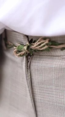 Ekose pantolonunda yeşil yapraklar ve sicimden yapılmış el yapımı kırsal bir kemerin makro çekimi. Dikey video.