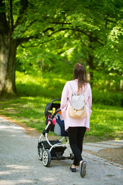 Mãe feliz andando com carrinho de bebê no parque — Fotografia de Stock