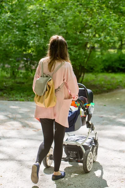 Gelukkig moeder wandelen met baby wandelwagen in park — Stockfoto