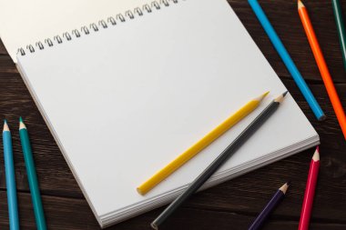 Eskiz defterini beyaz boş kağıtla aç. Beyaz çarşaftaki sarı ve gri kalem. Masada renkli kalemler var..