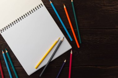 Eskiz defterini beyaz boş kağıtla aç. Beyaz çarşaftaki sarı ve gri kalem. Masadaki renkli kalemler. Uzayı kopyala Düz konum.