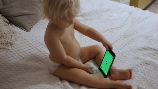 Portrait d'un mignon bébé vérifiant smartphone couché dans un lit — Video