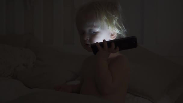 A portrait of a cute baby checking smartphone lying in a bed — Stock Video