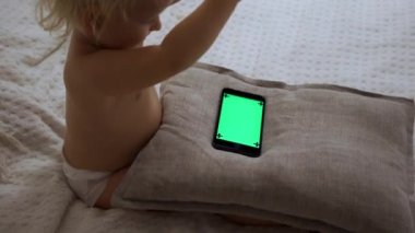 Yatakta uzanmış akıllı telefonu kontrol eden şirin bir bebeğin portresi.