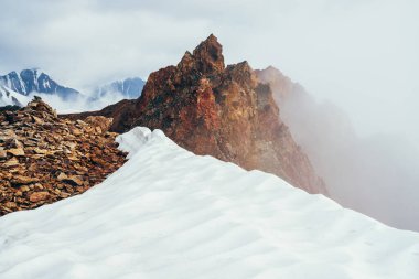 Dağda güzel, sivri kayalık tepeler ve kalın alçak bulutların arasında kar. Atmosferik minimalist alp manzarası. Keskin kayalık dağın tepesi, yoğun bulutların üstünde, uçurumda. Muhteşem dağlık manzara.
