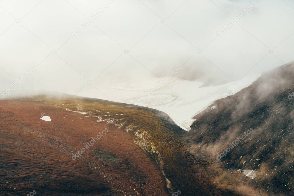 Atmospheric minimalist alpine landscape to highland valley with wide glacier on mountain slope inside cloud. Low clouds in rocky valley. Tranquil mountain scenery. Wonderful view to snowy mountainside