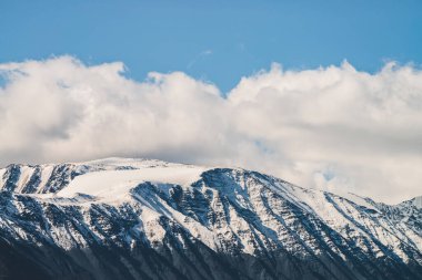 Atmosferik dağlık araziden güneşli bir günde karlı dağ sırtına. Dağların zirvesinde gün ışığında kar parlar. Güzel, parlak, karlı bluz. Karla kaplı alçak bulutlar için harika bir manzara.