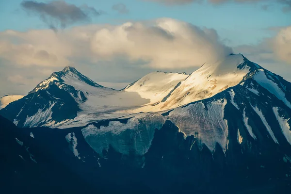 黄金の時間で低雲の間に大きな雪の山と大気高山の風景 日の出の巨大な山脈の巨大な氷河と素晴らしい高原の風景 大きな岩の上に輝く雪 — ストック写真