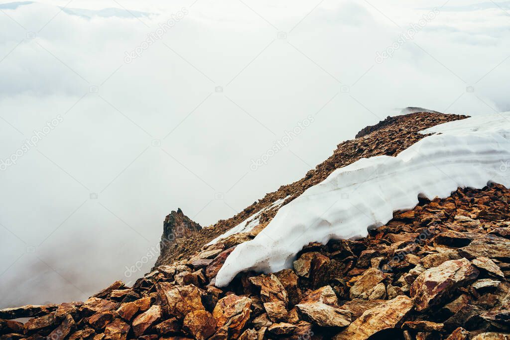Beautiful pointy cliff on high rocky mountain edge with snow among thick low clouds. Atmospheric minimalist alpine landscape. Pointed craggy stone near abyss in big cloud. Wonderful highland scenery.