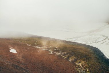 Atmosferik minimalist dağ manzarasından dağ yamacındaki geniş buzullu dağ vadisine kadar. Kayalık vadide alçak bulutlar. Huzurlu dağ manzarası. Karlı dağ yamacının harika manzarası