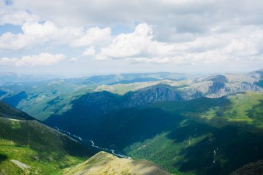 Dağ nehri ve ormanı olan manzaralı uzun vadinin sakin havası. Dev yeşil yamaçlardaki bulutların gölgeleri. Atmosferik alp manzarası ve uzun bir nehir. Yüksek irtifada görkemli manzara.