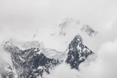 Atmosferik minimalist alp manzarası karlı dağ zirvesinde asılı devasa bir buzulla. Buzul sınırında büyük bir balkon. Karlı dağların arasında alçak bulutlar. Yüksek irtifada görkemli manzara.