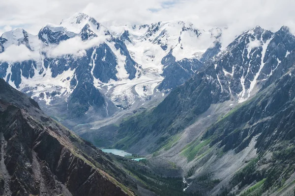 大气高山景观 巨大的冰川悬挂在巨大的岩石和山谷与山地湖泊 大冰川舌 白雪覆盖的高山上的低云 高空壮丽的风景 — 图库照片