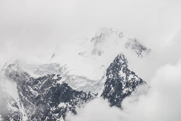 Atmospheric minimalist alpine landscape with massive hanging glacier on snowy mountain peak. Big balcony serac on glacial edge. Low clouds among snowbound mountains. Majestic scenery on high altitude.
