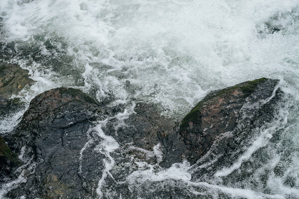 Full frame nature background with boulders in water riffle of mountain river. Powerful water stream of mountain creek. Textured backdrop of fast flow of mountain brook with rapids. Big stones close-up