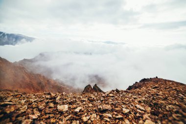 Uçurumun tepesindeki yüksek kayalık dağ yamacında alçak bulutlu güzel bir uçurum. Atmosferik minimalist alp manzarası. Bulutlardaki uçurumun kenarındaki sarp kayalıklar. Muhteşem dağlık manzara