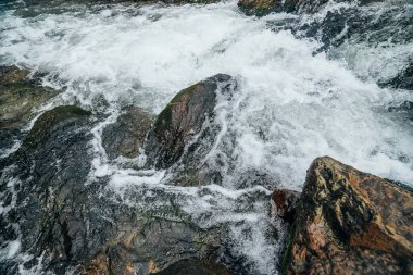 Dağ nehrinin su tabancasındaki kayalarla dolu tam bir çerçeve. Dağ deresinin güçlü su akıntısı. Dağ deresinin hızlı akışının desenli arkaplanı. Büyük taşlar yakın plan.