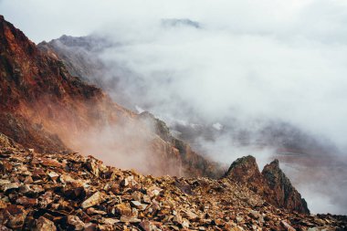 Uçurumun tepesindeki yüksek kayalık dağ yamacında alçak bulutlu güzel bir uçurum. Atmosferik minimalist alp manzarası. Bulutlardaki uçurumun kenarındaki sarp kayalıklar. Muhteşem dağlık manzara