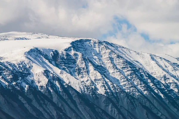Atmosferik dağlık araziden güneşli bir günde karlı dağ sırtına. Dağların zirvesinde gün ışığında kar parlar. Güzel, parlak, karlı bluz. Karla kaplı alçak bulutlar için harika bir manzara.
