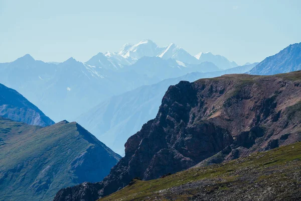 Derin vadinin arkasındaki büyük karlı dağların muhteşem manzarası. Devasa kayalıkları ve derin uçurumları olan harika dağ manzarası. Uzak mesafede büyük bir buzulla dağlık bir arazi. Büyük kayalar ve uçurumlar.