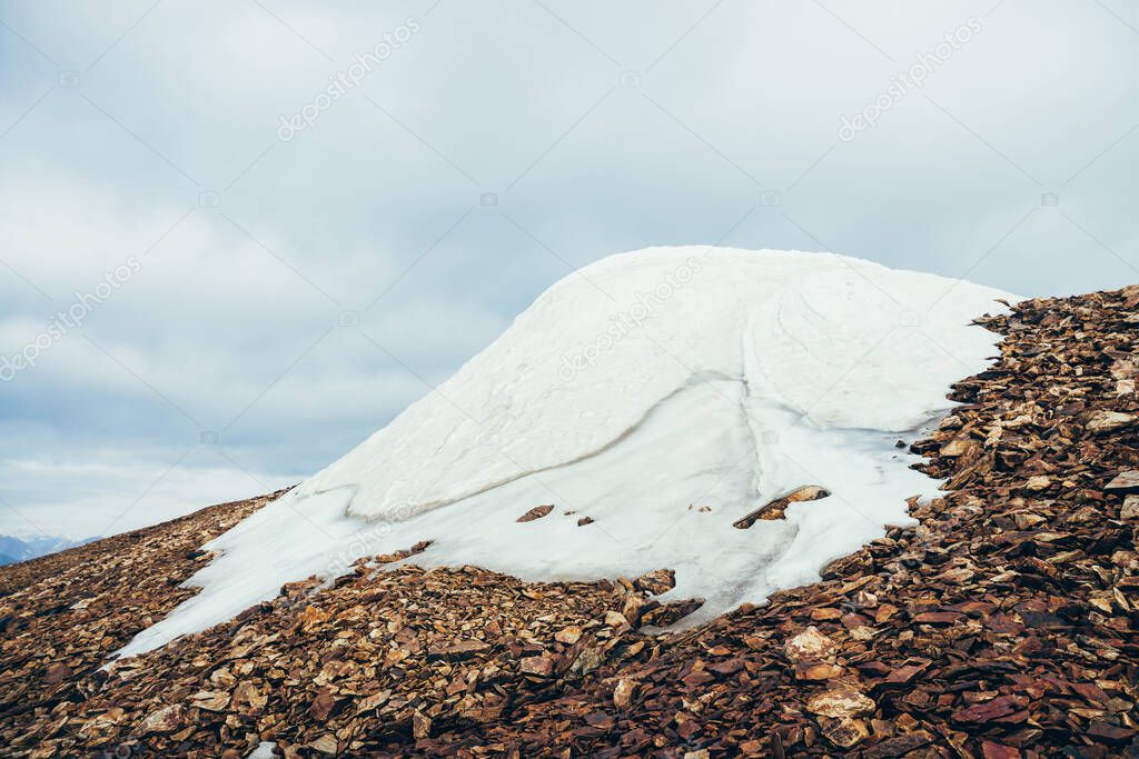 Large snowy dome on mountain top close-up. Firn on stony mountain peak on background of clouds. Snow on mountain on high altitude. Atmospheric minimalist alpine landscape. Wonderful highland scenery.