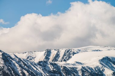 Atmosferik dağlık araziden güneşli bir günde karlı dağ sırtına. Dağların zirvesinde gün ışığında kar parlar. Güzel, parlak, karlı bluz. Karla kaplı alçak bulutlar için harika bir manzara.