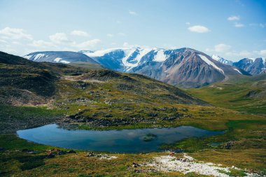 Manzaralı küçük alp gölü ve gün ışığında buzullu büyük dağlar. Güneşli bir günde yeşil dağlık vadideki yosunların arasında mavi dağ gölü olan muhteşem yeşil bir manzara. Harika manzara..