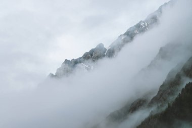 Bulutlu gökyüzündeki büyük uçuruma hayali atmosferik bir manzara. Dev kayalık dağların arasında alçak bulutlar. Sisli sabahın erken saatlerinde gizemli bir yer. Güzel kayalıkları olan minimalist bir manzara. Dramatik kasvetli sis.