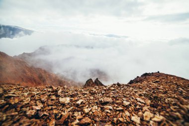 Uçurumun tepesindeki yüksek kayalık dağ yamacında alçak bulutlu güzel bir uçurum. Atmosferik minimalist alp manzarası. Bulutlardaki uçurumun kenarındaki sarp kayalıklar. Muhteşem dağlık manzara