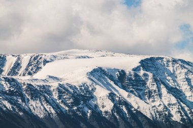 Atmosferik dağlık araziden güneşli bir günde karlı dağ sırtına. Dağların zirvesinde gün ışığında kar parlar. Güzel, parlak, karlı bluz. Karla kaplı alçak bulutlar için harika bir manzara.