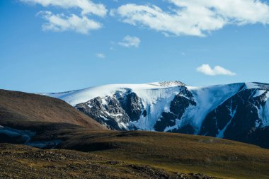 Yeşil tepenin arkasındaki karlı dağların muhteşem manzarası. Mavi gökyüzünün altındaki büyük buzullar. Karlı dev dağları olan muhteşem canlı dağlık bir manzara. Buzul dağlarıyla güzel dağ manzarası.