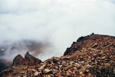 Uçurumun tepesindeki yüksek kayalık dağ yamacında alçak bulutlu güzel bir uçurum. Atmosferik minimalist alp manzarası. Bulutlardaki uçurumun kenarındaki sarp kayalıklar. Muhteşem dağlık manzara